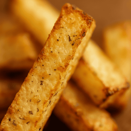Nahaufnahme einer knusprigen Kohlrabi-Pommes mit sichtbaren Kräutern und gebräunten Rändern