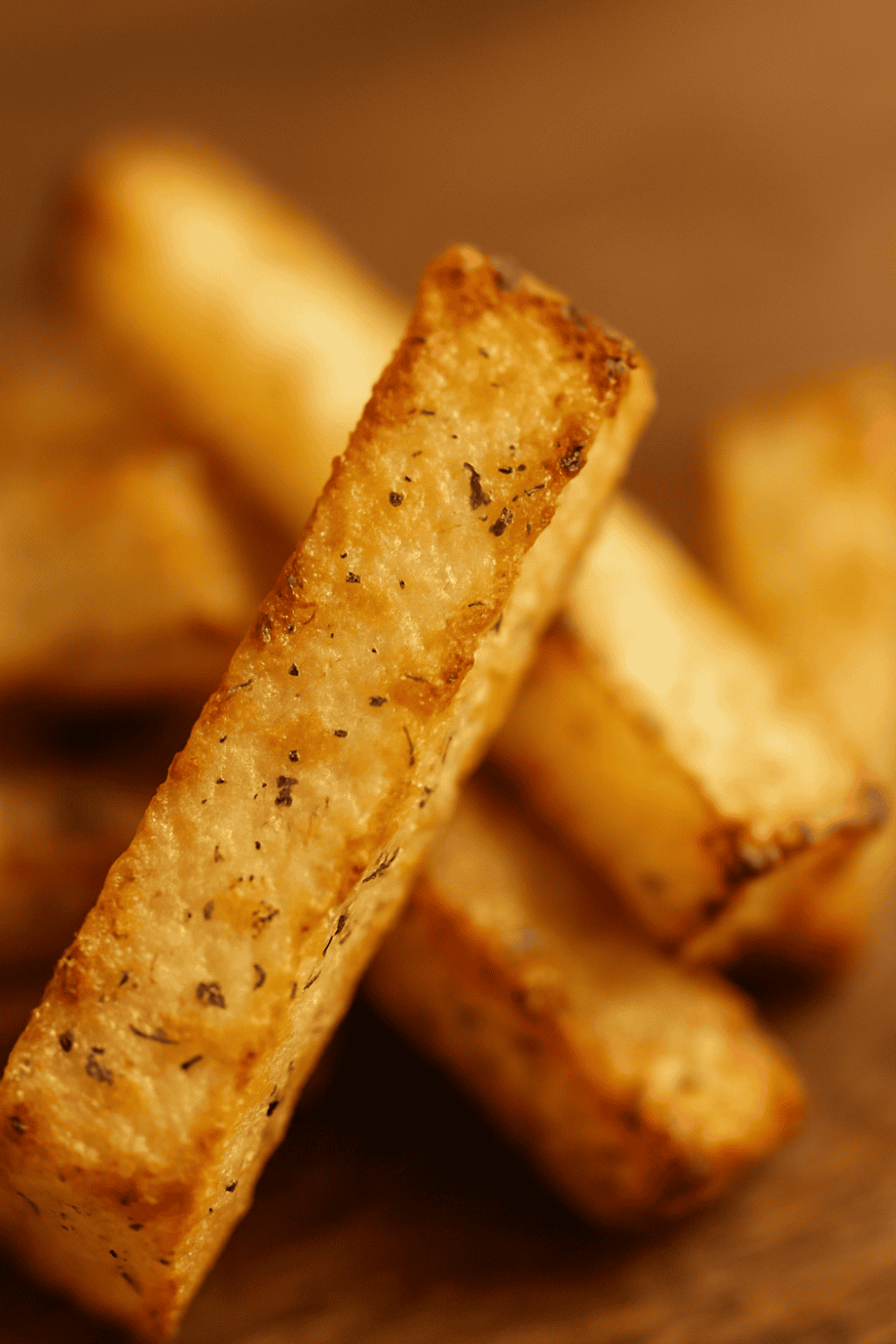 Nahaufnahme einer knusprigen Kohlrabi-Pommes mit sichtbaren Kräutern und gebräunten Rändern