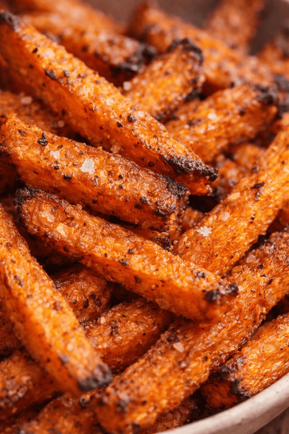 Nahaufnahme von knusprigen Süßkartoffel-Pommes mit sichtbarer Stärke-Kruste, karamellisierten Stellen und Gewürzen