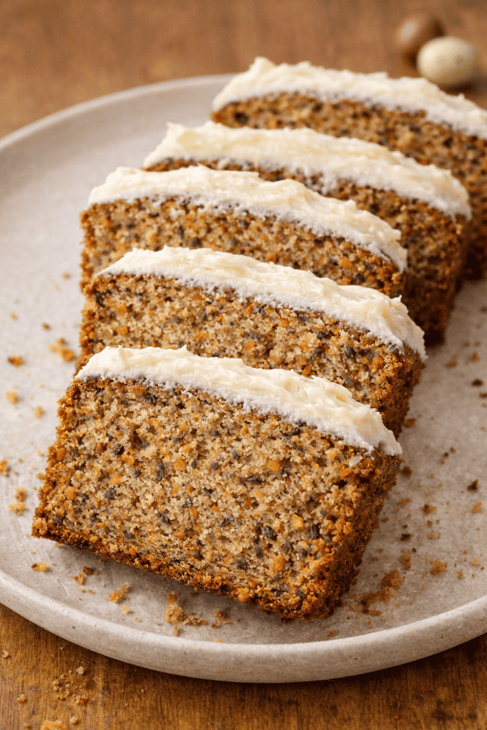 Mehrere Scheiben saftiger Karottenkuchen mit Frischkäse-Frosting auf weißem Teller, saftige Textur mit Nüssen und Karotten sichtbar