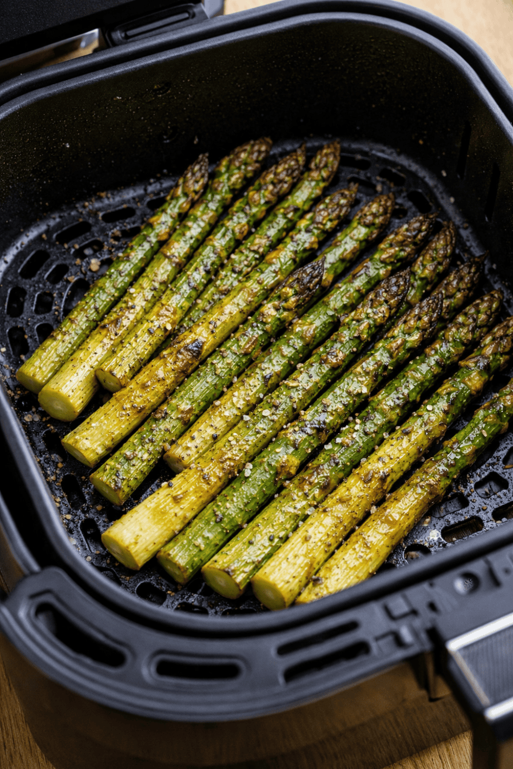 Grüner Spargel im Airfryer-Korb während der Zubereitung, gleichmäßig verteilt und gewürzt im schwarzen Fritteusenkorb