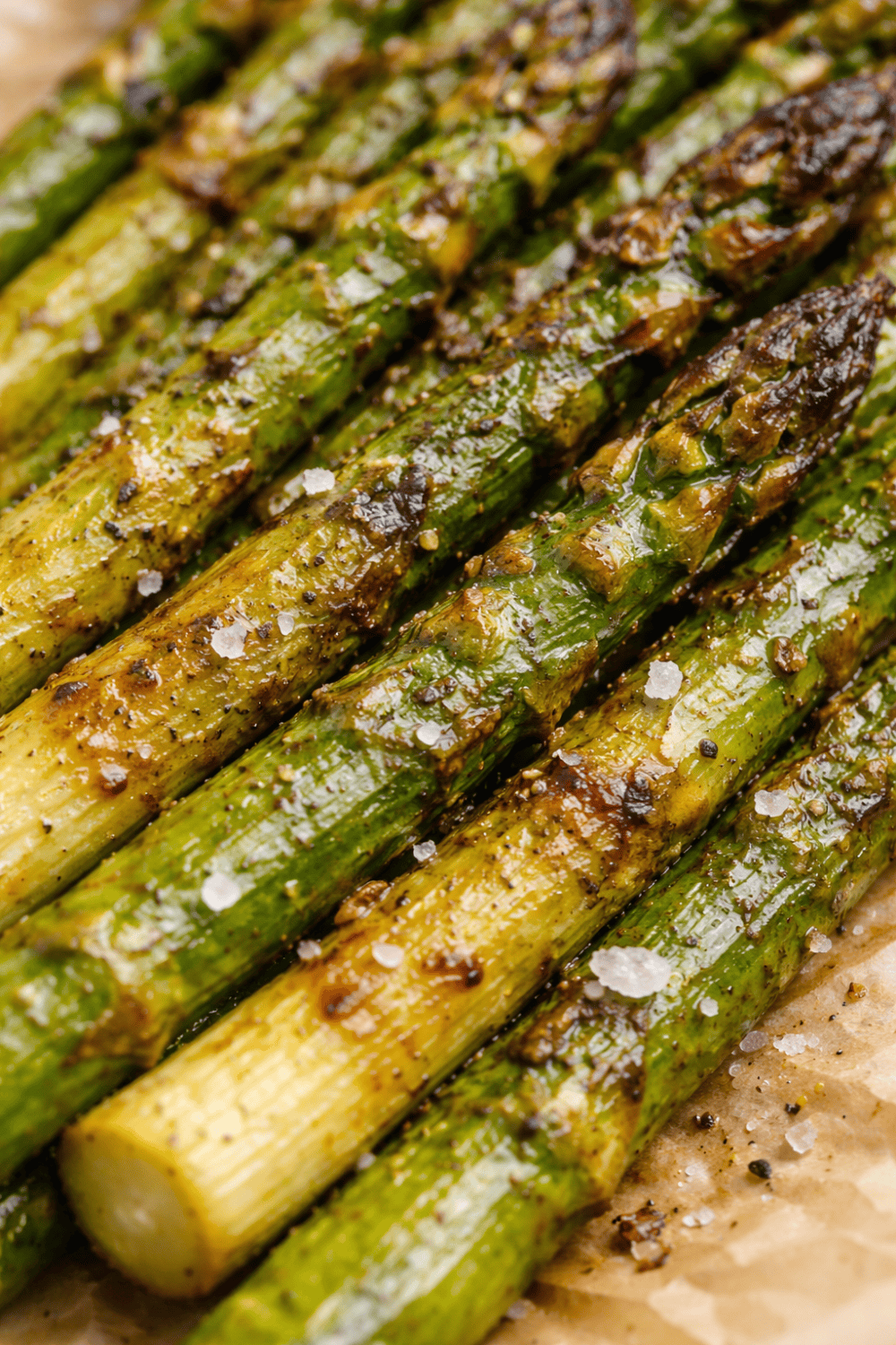 Nahaufnahme von geröstetem grünem Spargel mit sichtbaren Röstaromen, Olivenöl-Glanz und grobem Salz