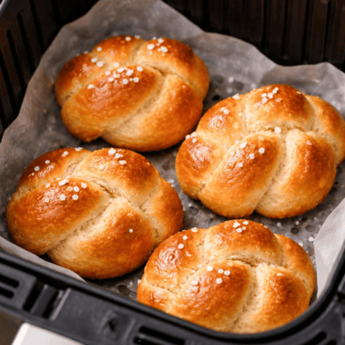 Vier frisch gebackene Mini-Hefezöpfe im Airfryer-Korb mit Backpapier, goldbraun glänzend, mit Hagelzucker bestreut