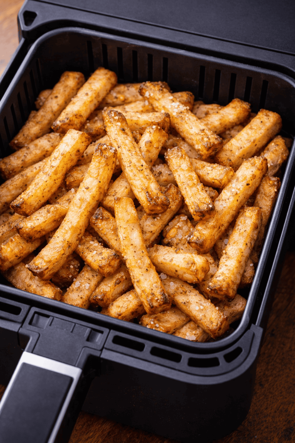 Frisch zubereitete Pommes selbstgemacht im schwarzen Korb der Heißluftfritteuse, goldbraun gegart mit Paprika-Gewürzmischung