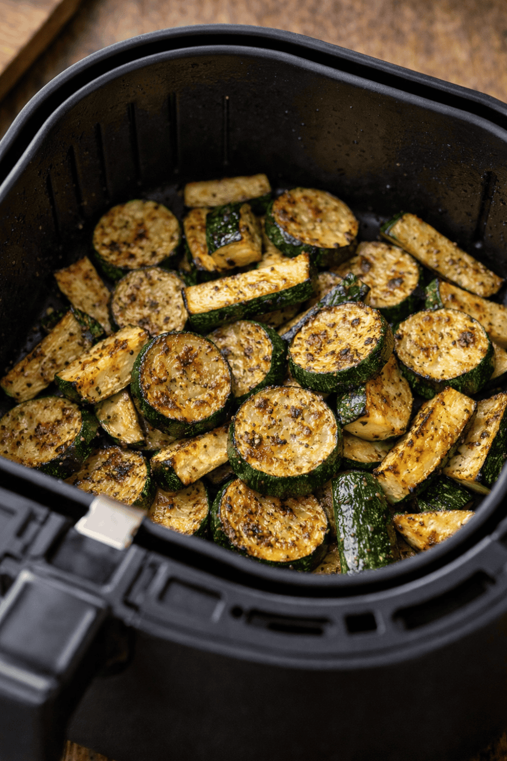 Gewürzte Zucchini-Scheiben und Zucchini-Sticks während des Garens im schwarzen Airfryer-Korb mit beginnenden Röstaromen und gleichmäßiger Verteilung