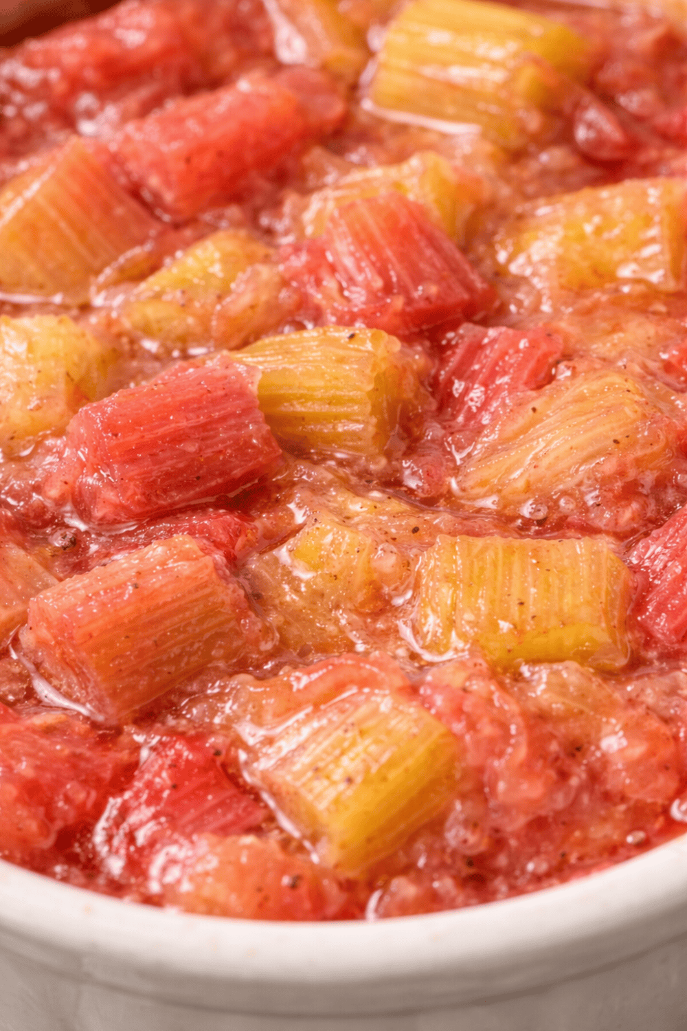 Nahaufnahme Rhabarberkompott mit weichen, glänzenden Rhabarberstücken in Rot- und Gelbtönen, sichtbare Vanilleflecken, saftig