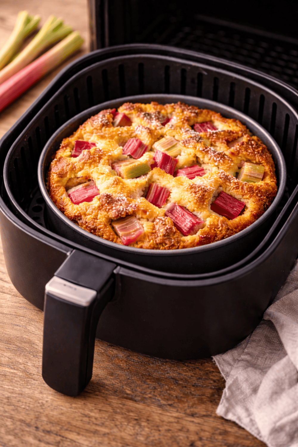 Rhabarberkuchen in einer runden Backform im Korb der Heißluftfritteuse – goldbraun gebacken mit sichtbaren Rhabarberstücken