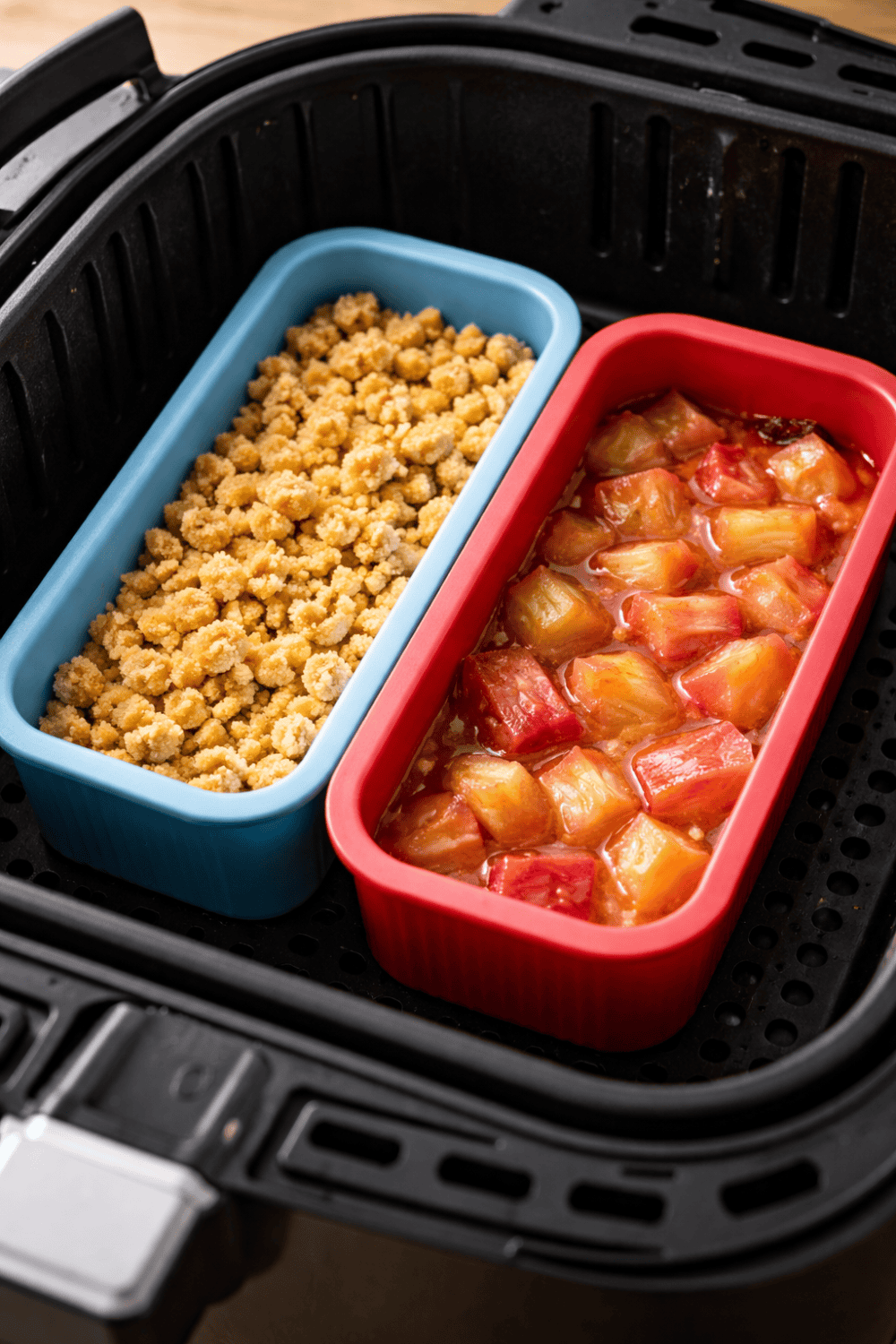 Zwei Silikonformen im Airfryer-Korb – blaue Form mit rohen Streuseln und rote Form mit geröstetem Rhabarber aus der Heißluftfritteuse