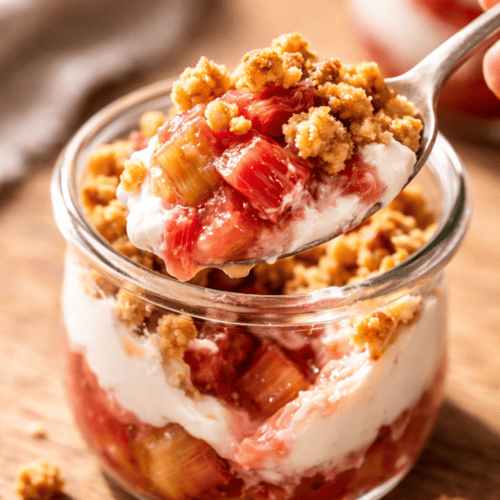 Löffel mit einem Bissen Rhabarber-Schicht-Dessert aus dem Glas – mit Quarkcreme, geröstetem Rhabarber und Streusel-Crunch aus der Heißluftfritteuse