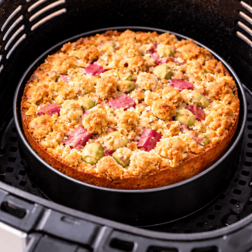 Rhabarber-Streuselkuchen in einer runden Backform Ø 18 cm im Korb einer weißen Heißluftfritteuse – fertig gebacken mit knusprigen Streuseln.