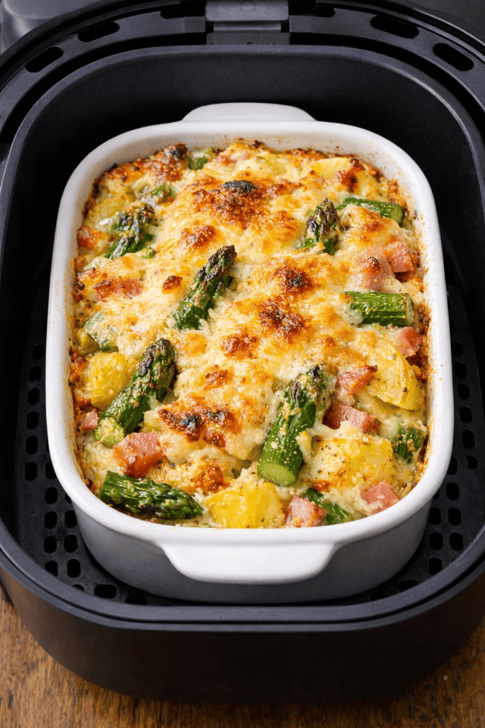Spargel-Auflauf in kleiner Auflaufform im Airfryer-Korb, überbacken mit Käse, Kartoffeln und grünem Spargel sichtbar