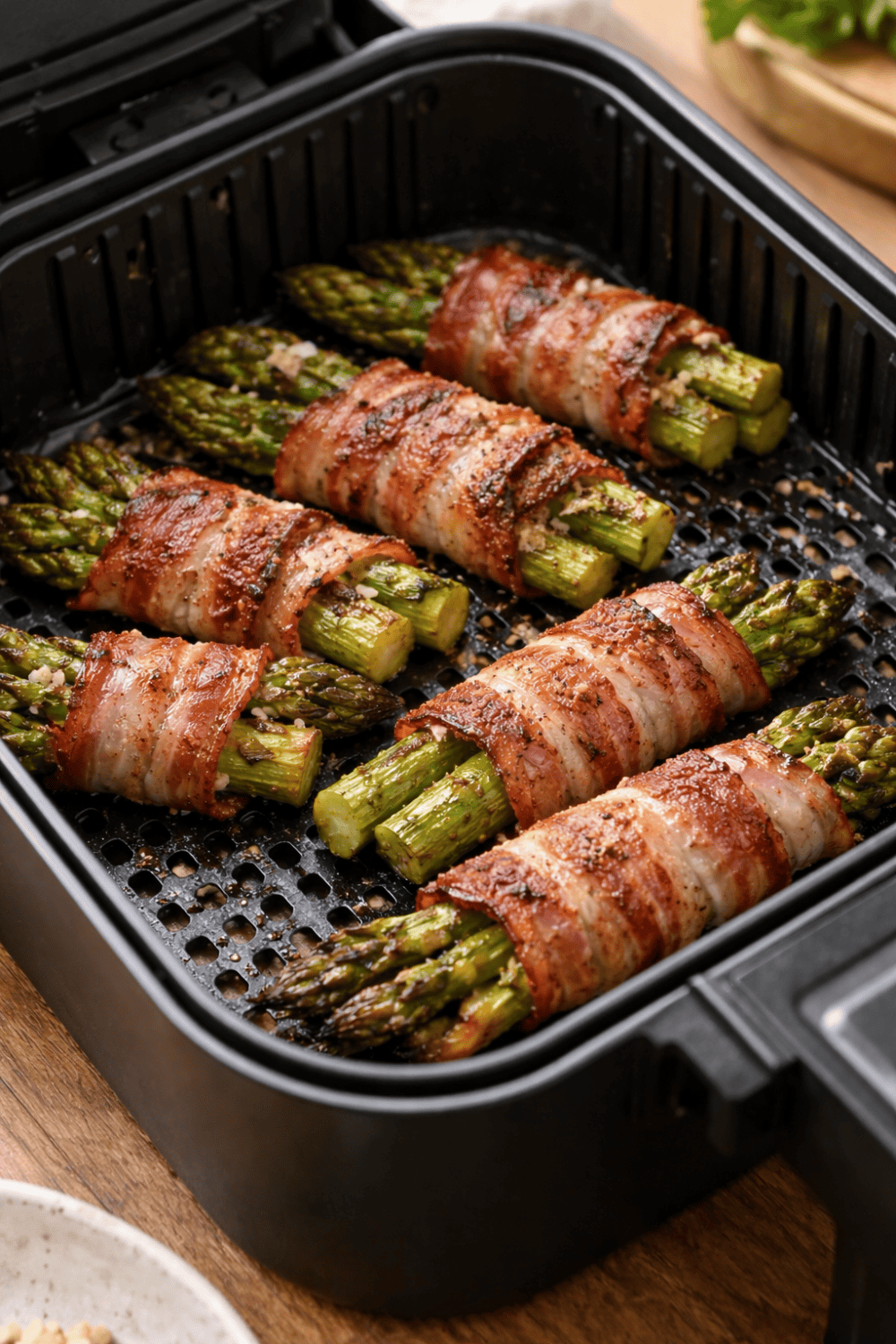 Grüner Spargel mit Bacon umwickelt im Airfryer-Korb beim Garen